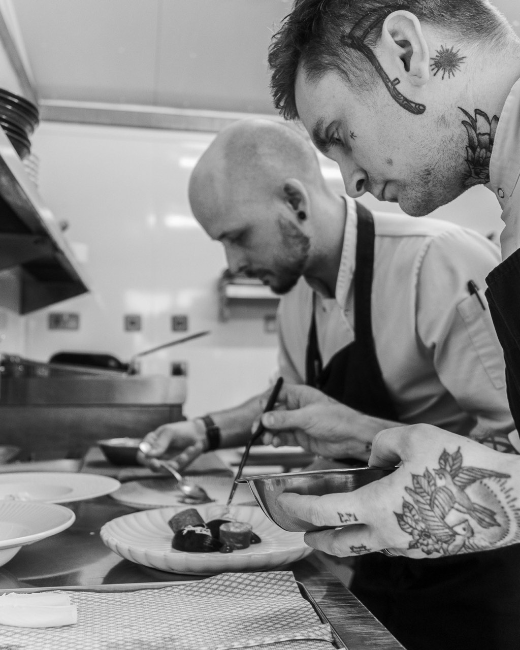 Black-and-white photograph of the kitchen team plating dishes during service at The Peacock Inn