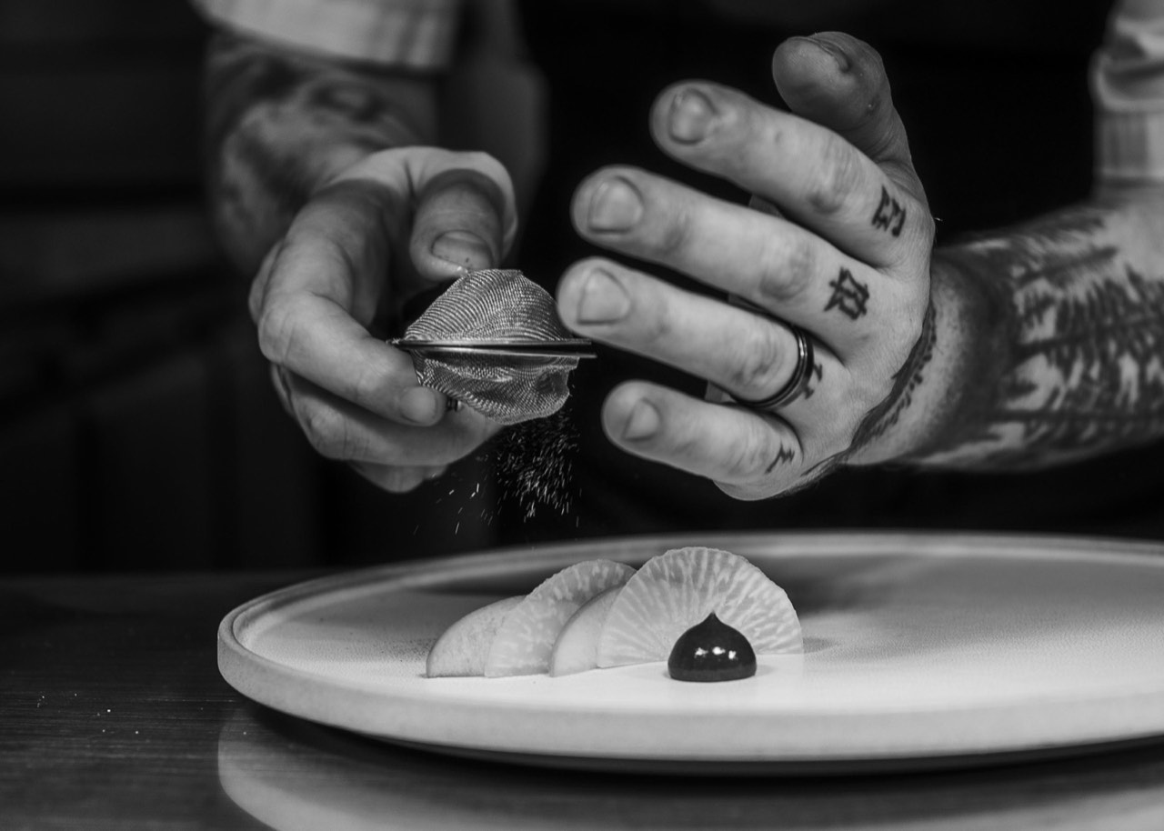 A chef's hands finishing a plated dish in the kitchen at The Peacock Inn