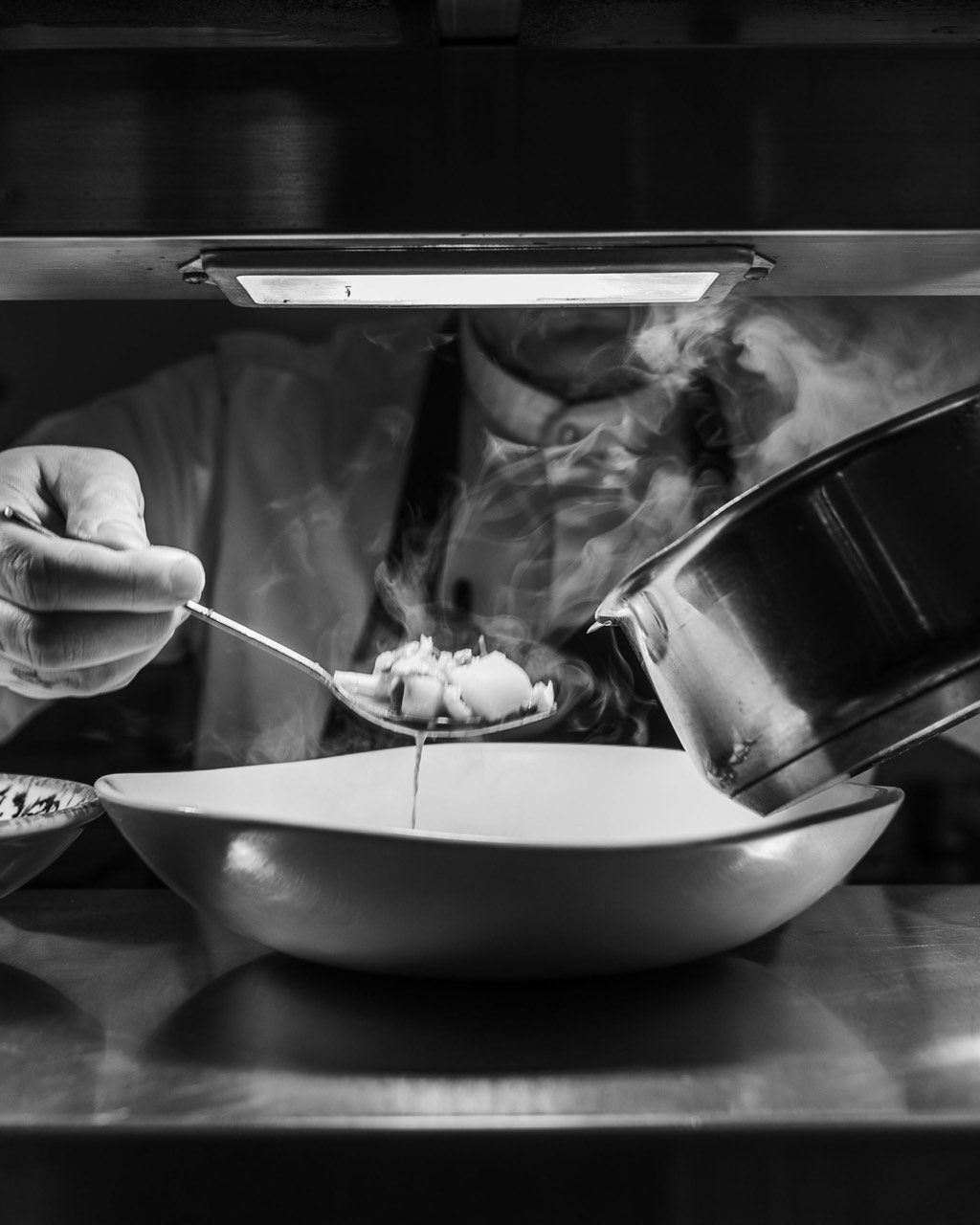 Black-and-white photograph of a chef's hands carefully dressing a dish at The Peacock Inn